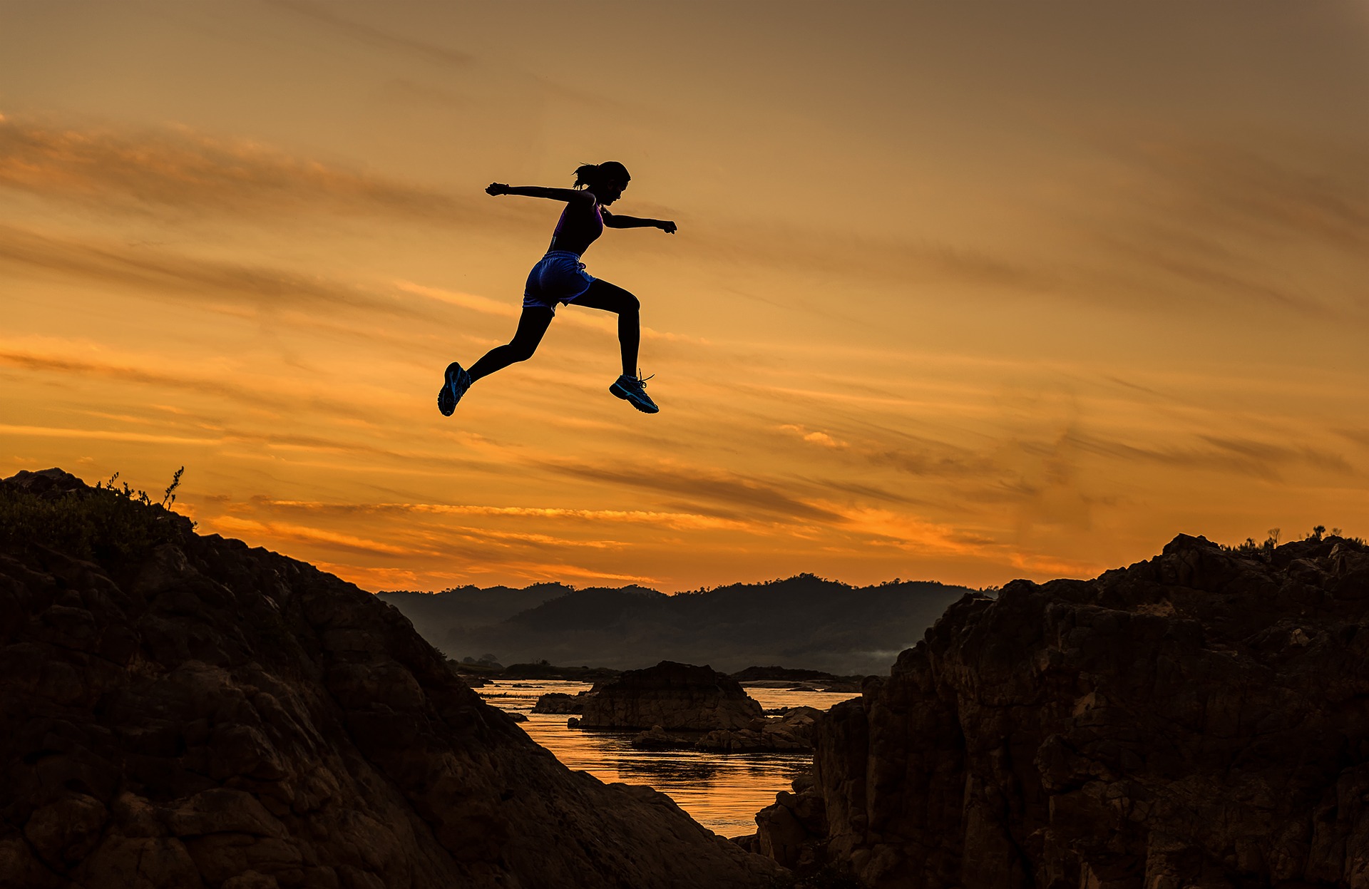 a female athlete jumping across a ridge