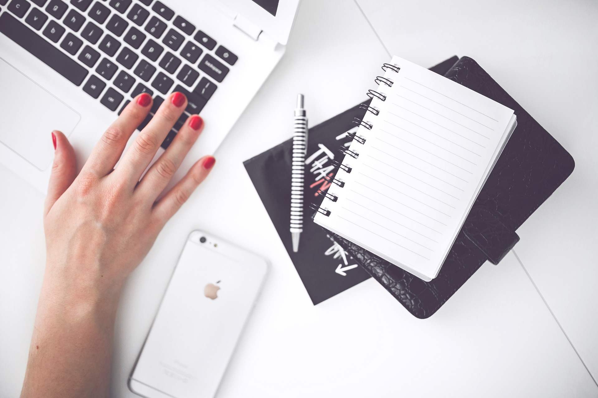 a female hand working on a laptop with a notebook, pen, mobile phone nearby