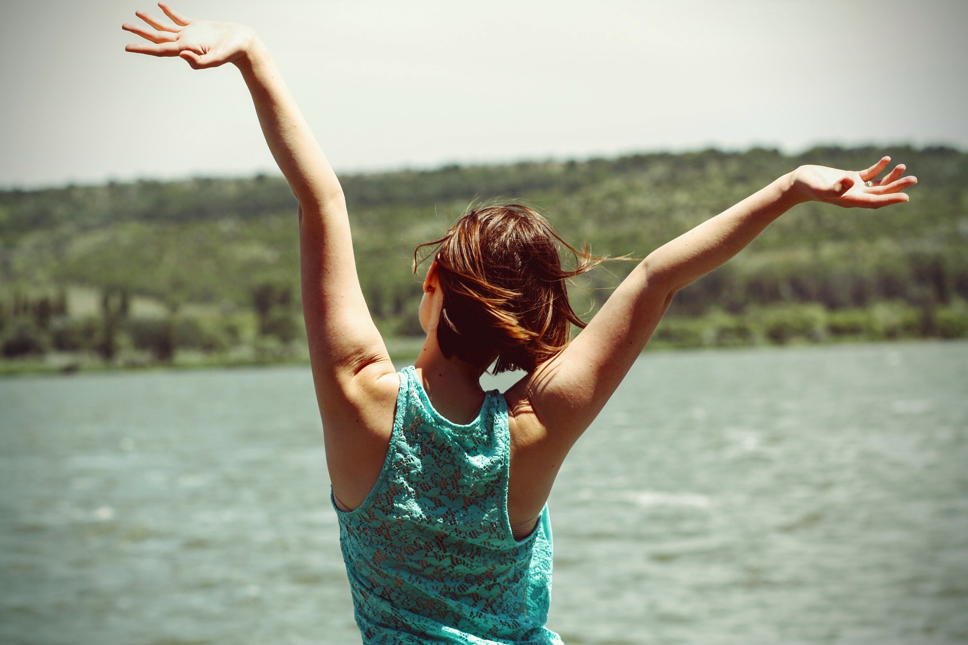 a girl in a cheerful mood standing in front of a lake with her arms stretched